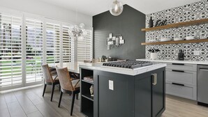 A modern kitchen with a central island, white cabinetry, and a black backsplash. - GATED, Spacious 2-bedroom condo in Indian Wells close to restaurants and more. (Indian Wells)