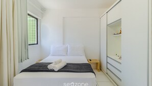 Una habitación de hotel con una cama, una mesita de noche pequeña, un espejo y una ventana con cortinas.