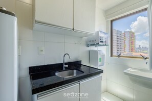 A modern kitchen with a black countertop, stainless steel sink, and white cabinets. There is a window with a view of a cityscape. - Near the sea and the Best of Recife! Cav0411 (Recife)