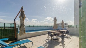 Un área de piscina en la azotea con sillas reclinables azules, una piscina y sombrillas.