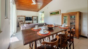 Un comedor con una mesa de madera dispuesta para cuatro personas, rodeada de sillas. Un televisor está montado en la pared, y se observa un armario al fondo.