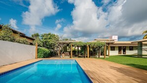 Una piscina con cubierta de madera, rodeada por un jardín y un edificio con tejado de baldosas.