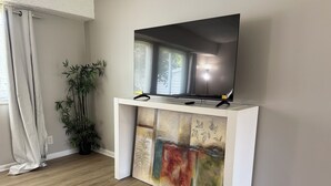Ein Wohnzimmer mit einem Flachbildfernseher auf einer weißen Konsole, einer Topfpflanze und einem Gemälde auf der Konsole.