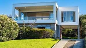 Una casa moderna de dos pisos con techo plano, ventanas amplias y un césped bien cuidado.