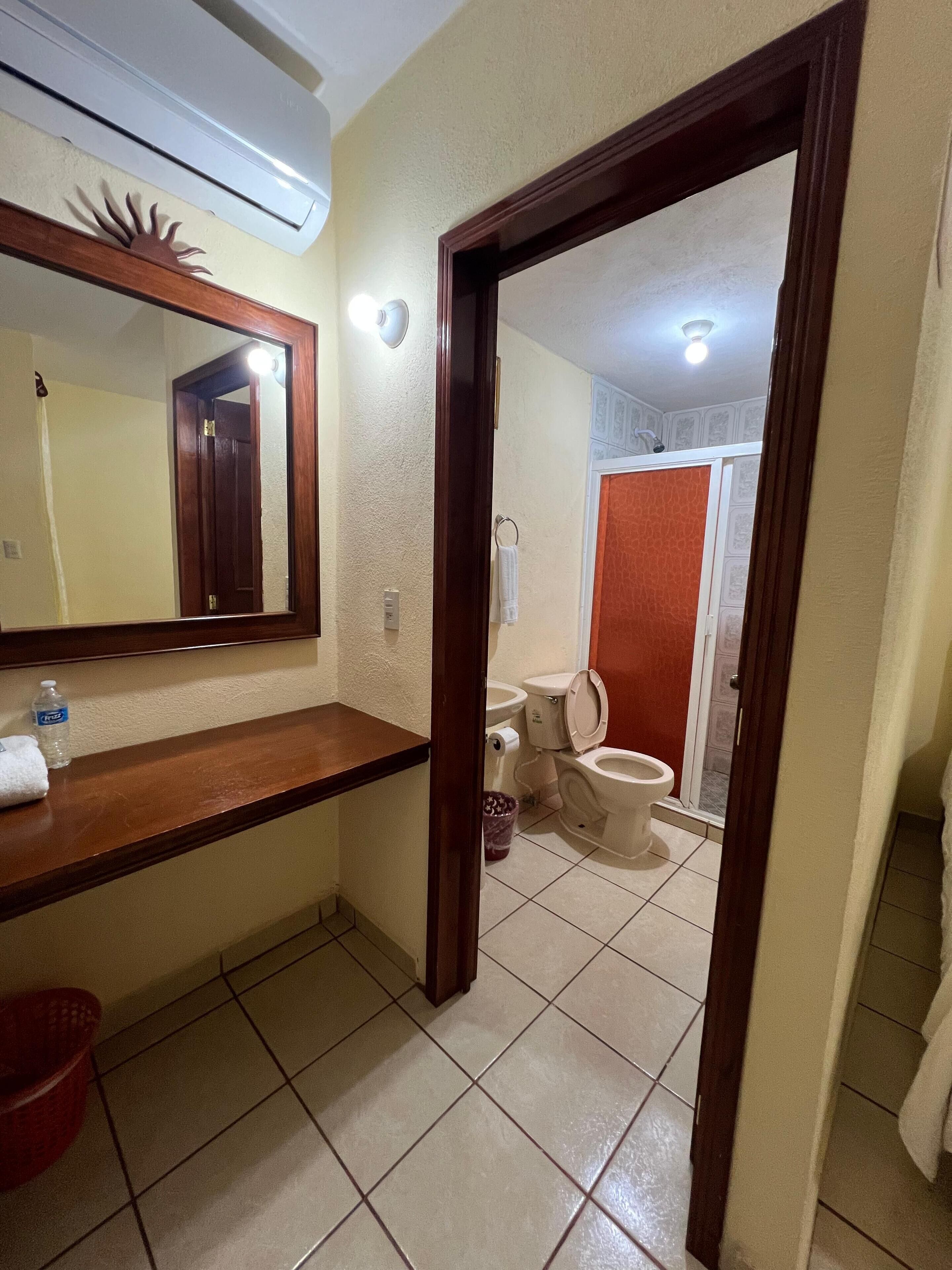 Un baño con tocador de madera, un espejo, una toalla, una botella de agua y un inodoro.