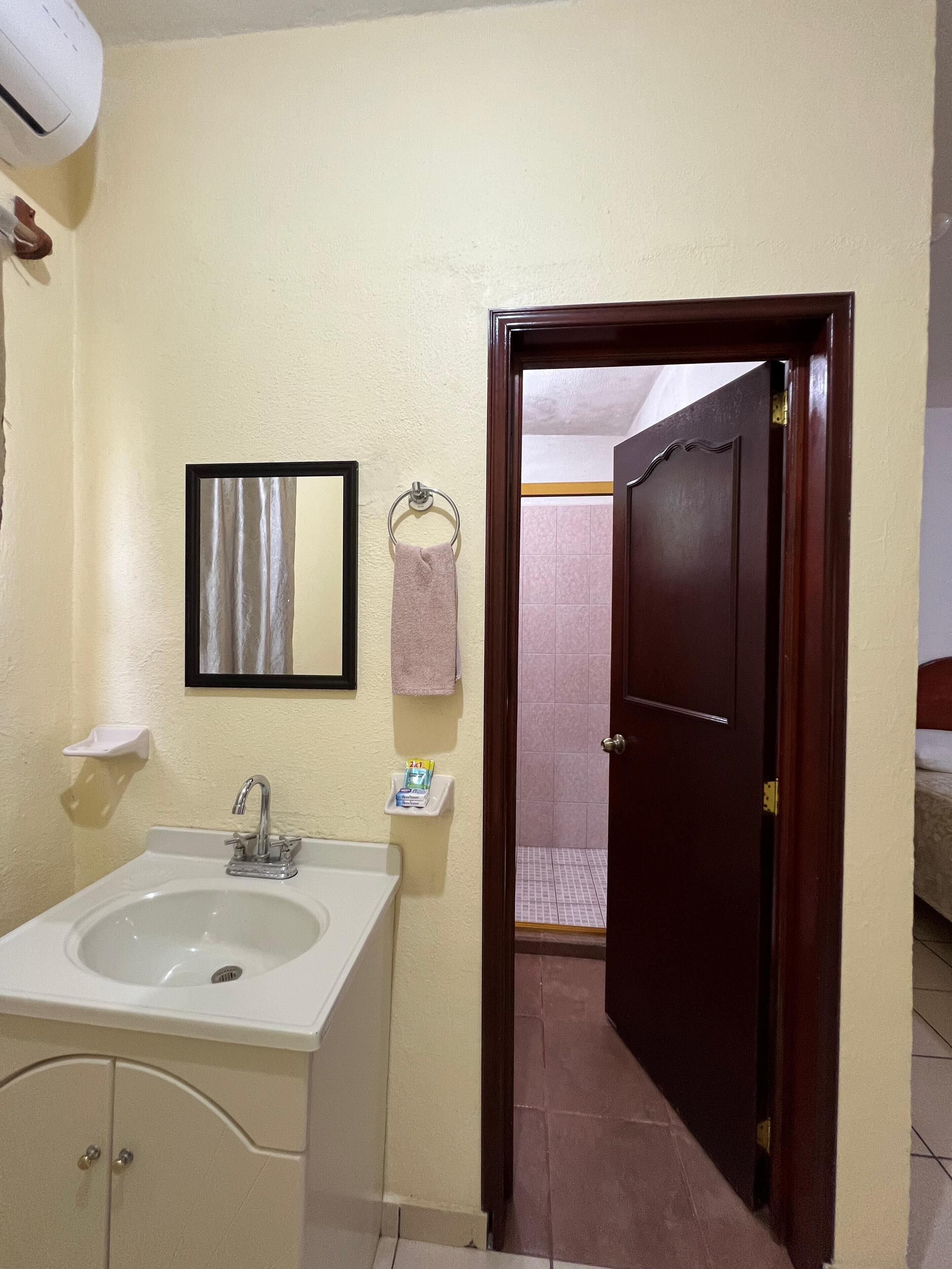 Casa de banho com lavatório, espelho, porta-toalhas e porta de acesso à área de duche.