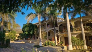 A multi-story hotel with balconies, palm trees, and a cobblestone pathway. - HOTEL Y RESTAURANTE VILLAS DEL SOL (Jalpan de Serra)