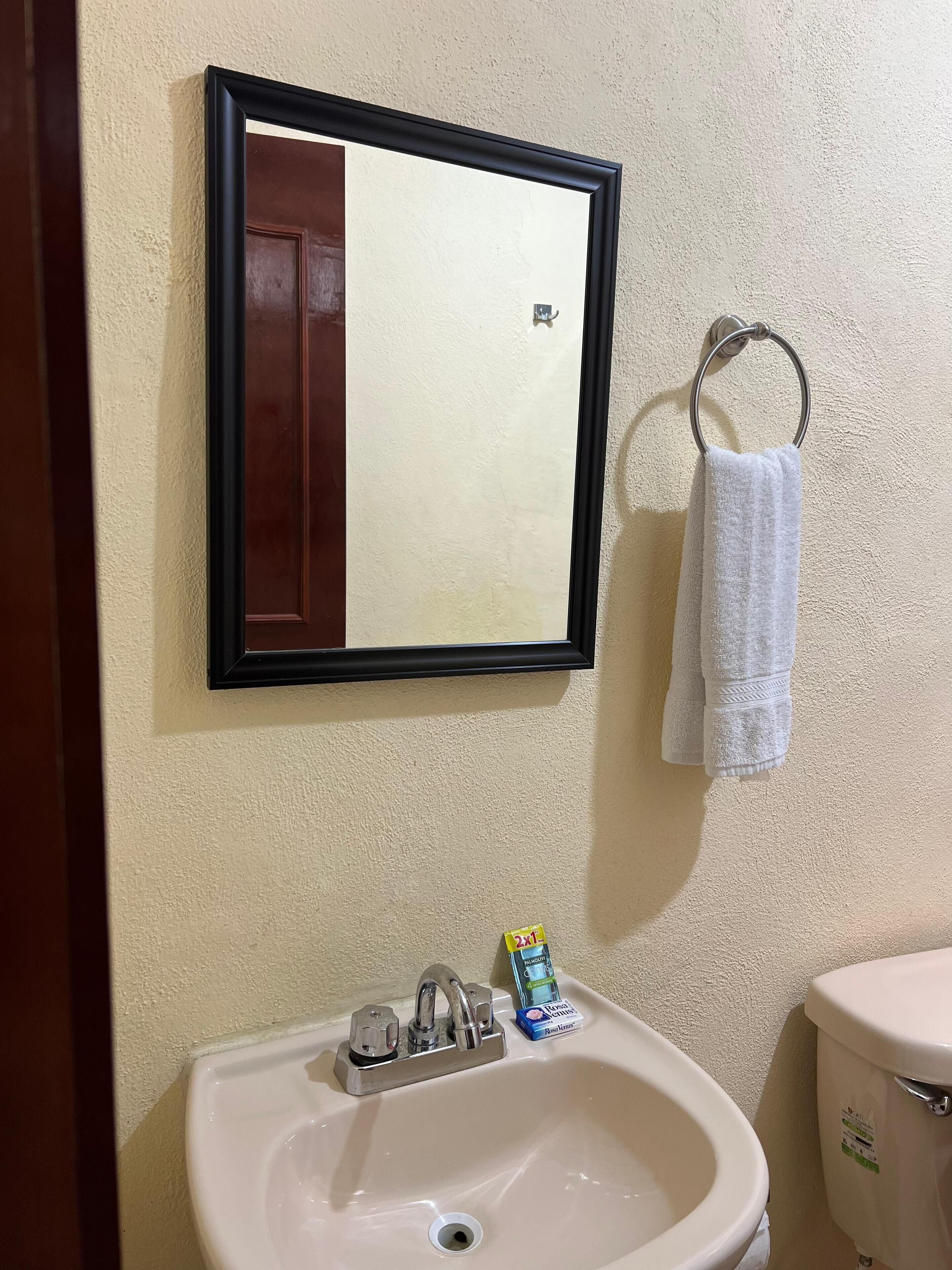 Ein Badezimmer mit Waschbecken, Spiegel, Handtuchhalter und Toilette.