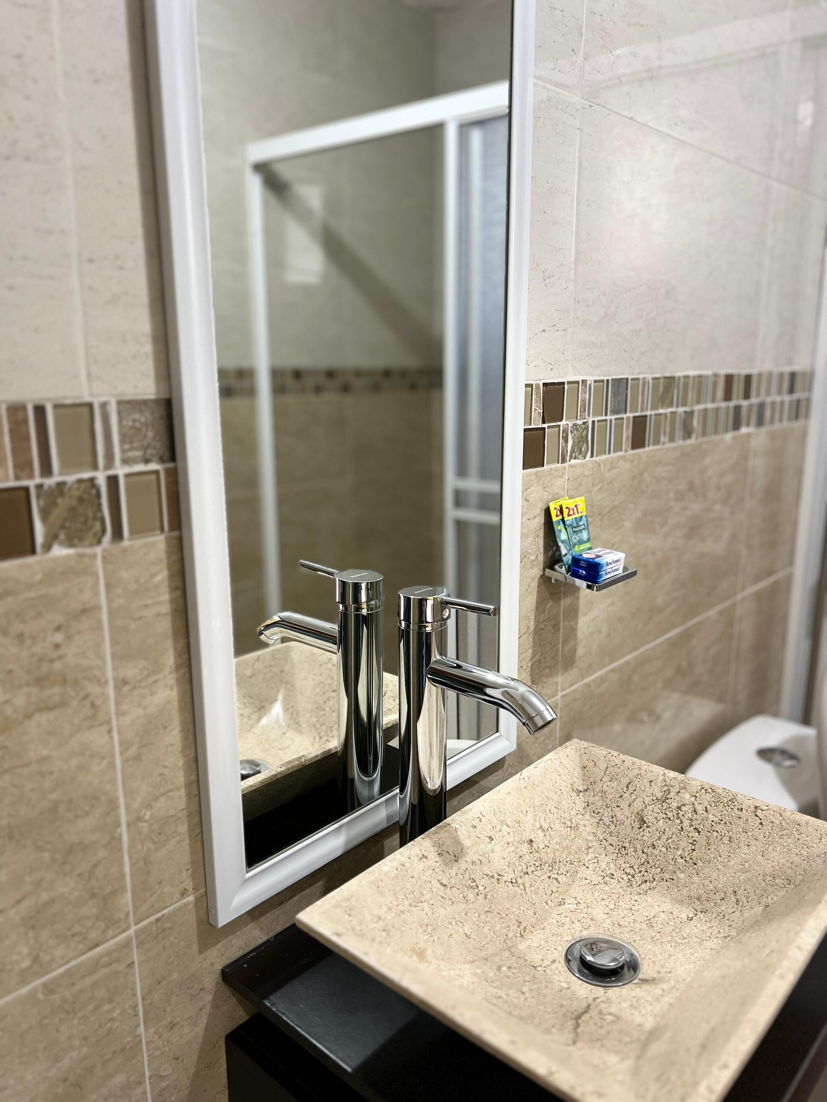 A bathroom with a rectangular sink, chrome faucets, and a mirror.
