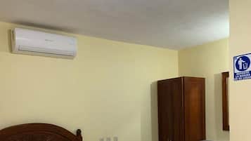 Habitación de hotel con una cama, un armario de madera, un escritorio con espejo y un cesto de basura.