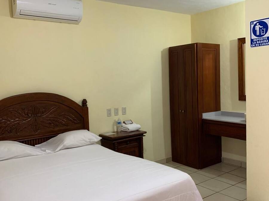 Habitación de hotel con una cama, un armario de madera, un escritorio con espejo y un cesto de basura.