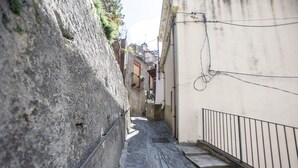 A narrow cobblestone alley with stone walls on one side and a white building with a metal railing on the other. - House in the mountains near the sea (Itala)