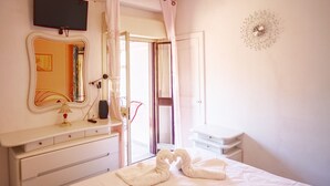 A hotel room with a bed, a vanity with a mirror, a flat-screen TV, a bedside table with a lamp, and a wall clock. - House in the mountains near the sea (Itala)