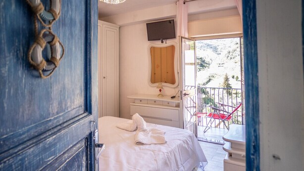A bedroom with a bed, a bedside table, a mirror, and a balcony with red chairs. - House in the mountains near the sea (Itala)