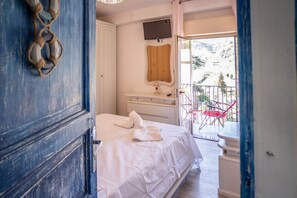 Un dormitorio con cama, mesita de noche, espejo y balcón con sillas rojas.
