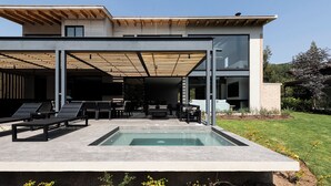 Ein modernes Haus mit Pool, Außenbereich mit Sitzgelegenheiten und einer überdachten Terrasse.
