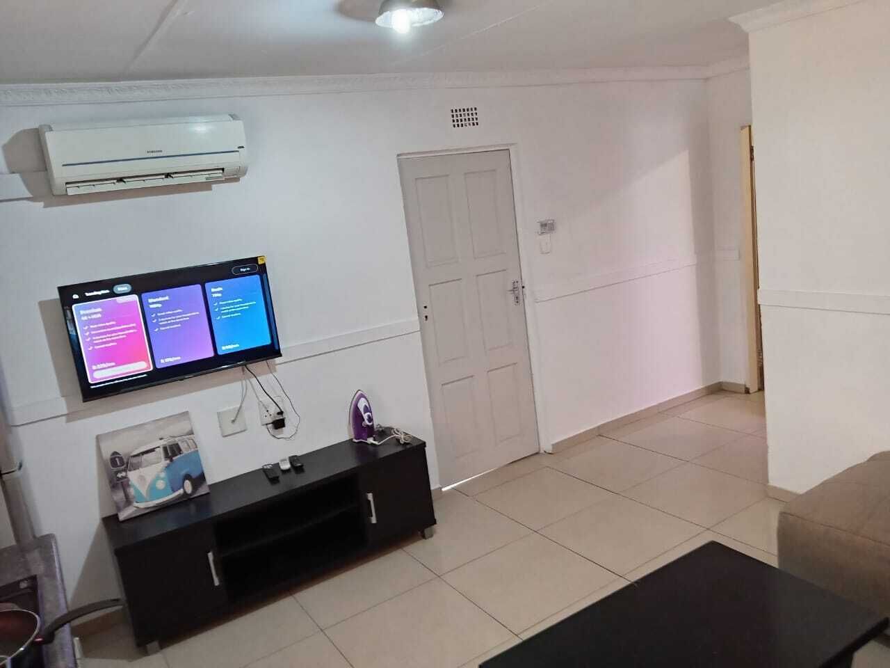 A room with a flat-screen TV mounted on the wall, a white door, and a tiled floor.