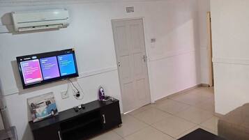 A room with a flat-screen TV mounted on the wall, a white door, and a tiled floor.