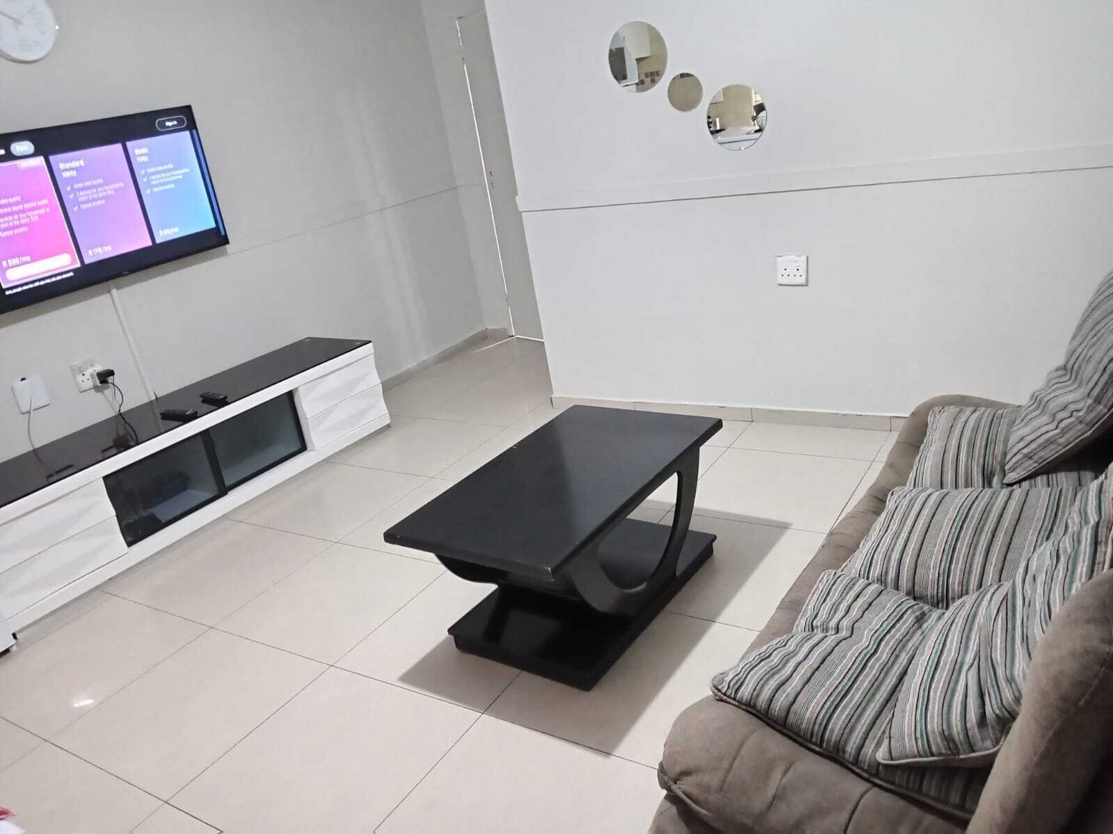A modern living room with a flat-screen TV mounted on the wall, a black coffee table, a sofa, and a white entertainment unit.