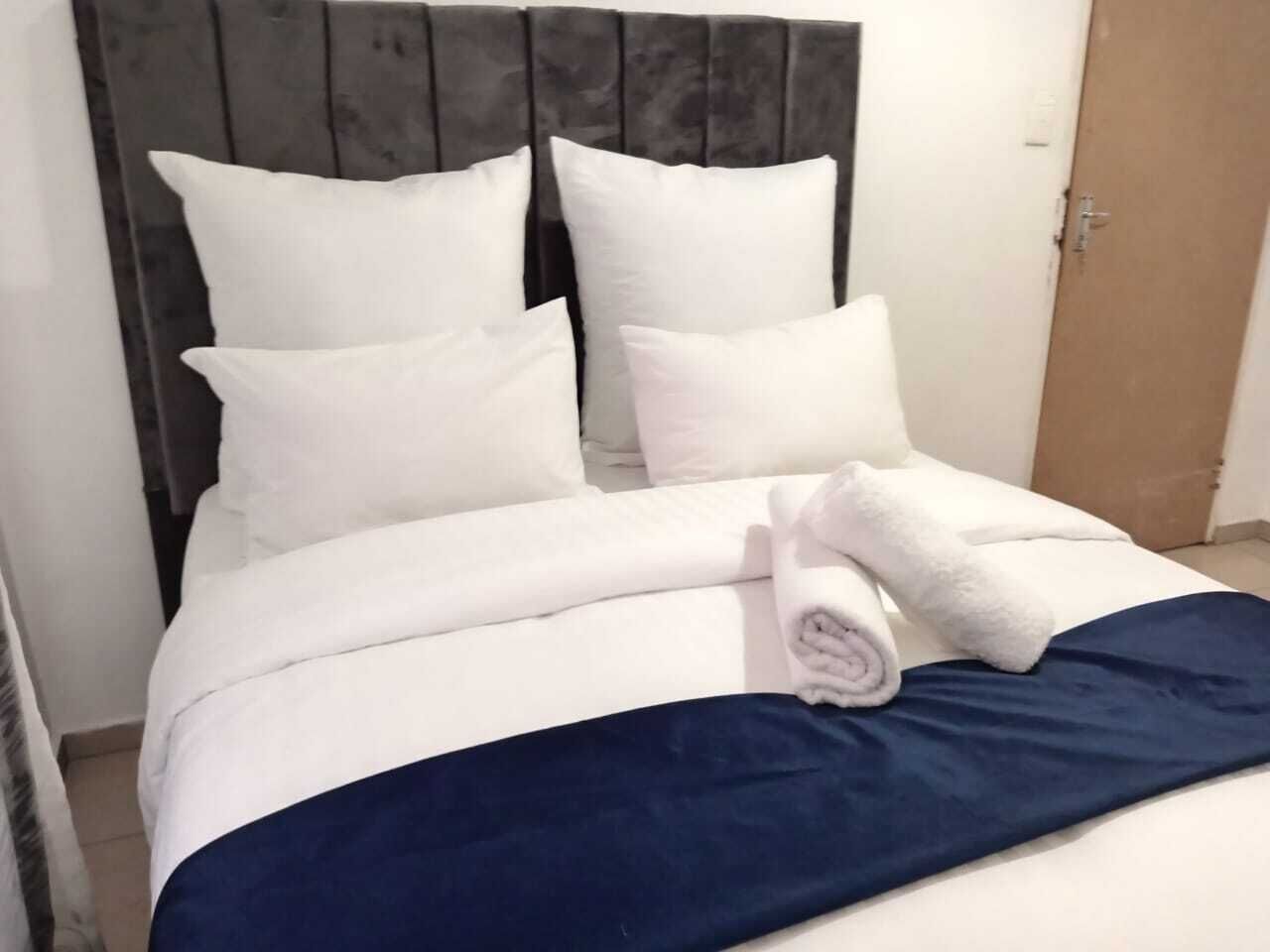 Een opgemaakt bed met witte lakens en een donkerblauwe deken, een houten hoofdbord en een witte handdoek op het bed.