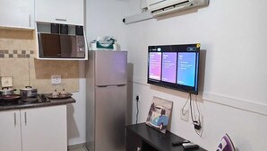 A compact kitchen with a microwave, refrigerator, and a flat-screen TV mounted on the wall.