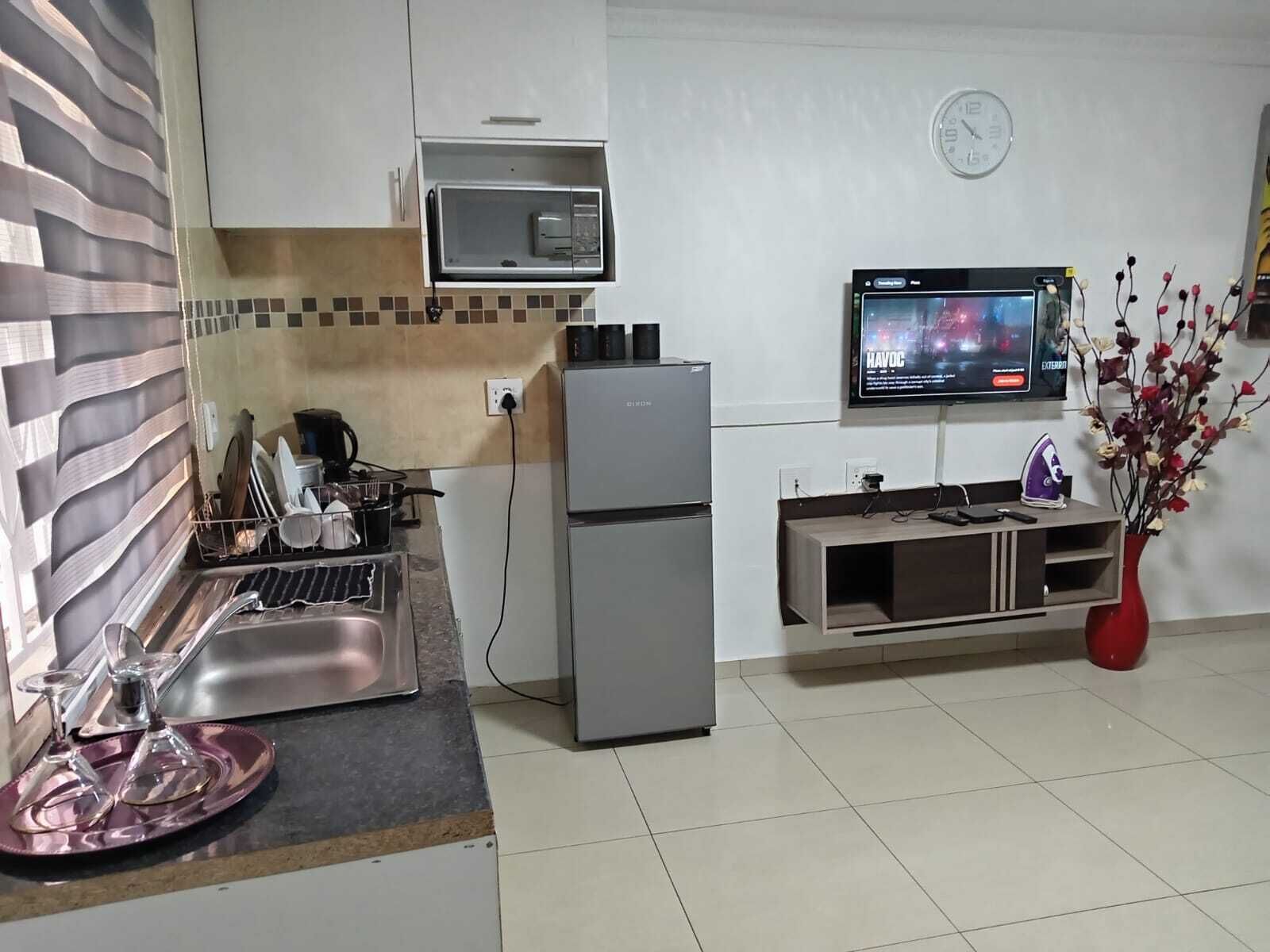 A compact kitchen with a microwave, a refrigerator, a sink, and a television mounted on the wall.