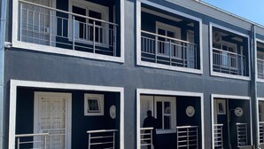 A multi-story building with balconies, a concrete ground floor, and a series of doors and windows.