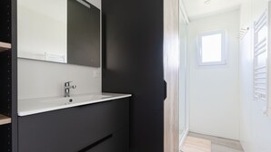 Ein modernes Badezimmer mit einem weißen Waschbecken, dunklen Schränken und einem großen Spiegel.