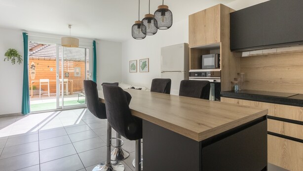 A modern kitchen with a wooden island, black chairs, and a hanging light fixture.