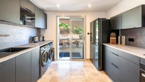 A modern kitchen with a built-in washer and dryer, a large refrigerator, and a sliding glass door leading to an outdoor patio.