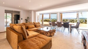 A modern living room with a sectional sofa, a glass coffee table, and a dining area with chairs and a table.