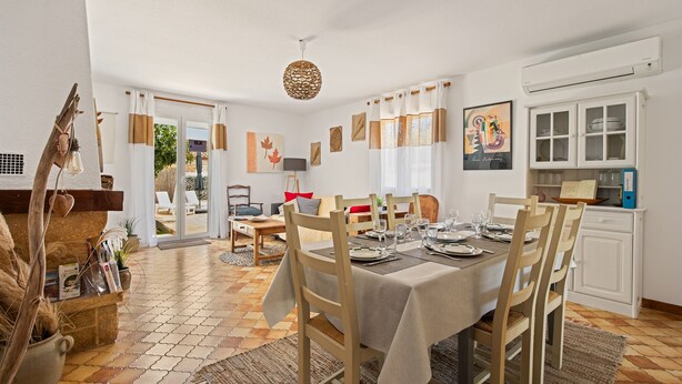 Un coin repas avec une table dressée pour quatre personnes, entouré de chaises en bois, un sol à motifs et une vue sur l’extérieur grâce à des portes vitrées.