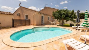 Une piscine avec une terrasse carrelée, un patio couvert avec des chaises et un bâtiment doté d’un toit en tuiles.