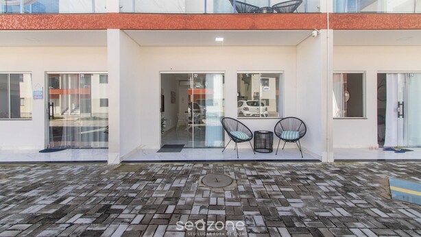 A modern building with a brick-paved entrance, glass doors, and a seating area with chairs.