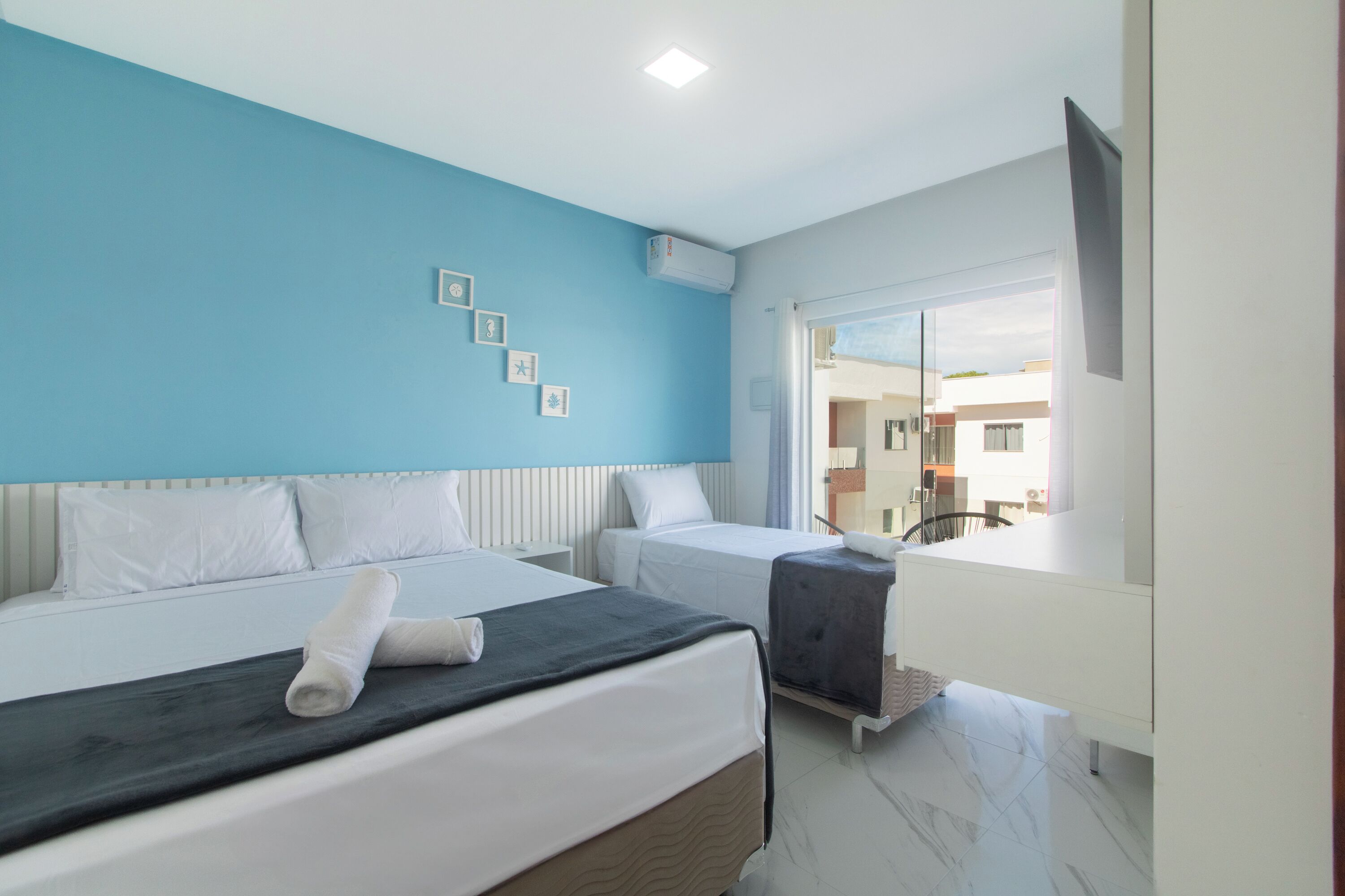 Hotelkamer met twee bedden, een blauwe accentmuur, een groot raam en uitzicht op buiten.