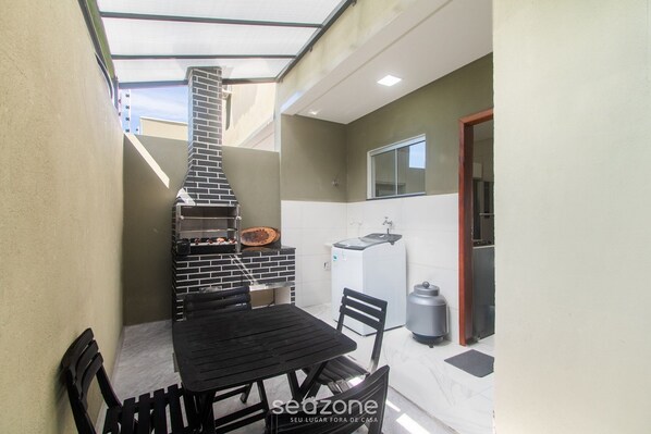 A compact kitchen with a brick oven, a dining table, and chairs. - Stay With Pool Just Minutes From the Beach - CCR (Porto Seguro)