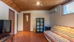 A room with a wooden ceiling, a television, a sofa, a bookshelf, and a window. - La Bouscarle - Jardin et Piscine Partagée (Châteaudouble)