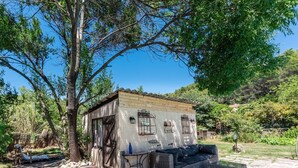 A rustic cabin with a wooden exterior, a small porch, and a wicker sofa. - La Bouscarle - Jardin et Piscine Partagée (Châteaudouble)