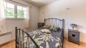 A bedroom with a bed, a nightstand, a window with curtains, and a radiator. - La Bouscarle - Jardin et Piscine Partagée (Châteaudouble)