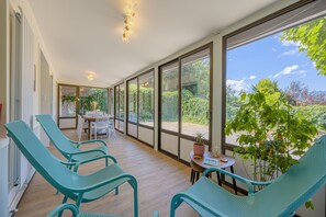 Una habitación iluminada por el sol, con ventanas amplias, sillas color turquesa, una mesita y una planta en maceta.