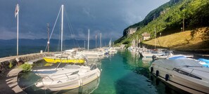 A marina with boats docked, a stone wall, and a hillside with vegetation.