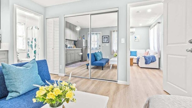 A modern living room with a blue sofa, a coffee table with a vase of flowers, and a sliding glass door leading to a kitchen and dining area.