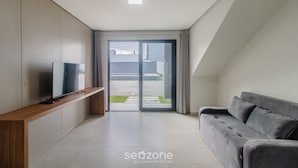 A modern living room with a flat-screen TV on a wooden console, a grey sofa, and a sliding glass door leading to an outdoor area. - Apartments With Swimming Pool 700m From Taperapuan Beach Nvm0009 (Porto Seguro)
