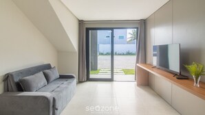 A modern living room with a grey sofa, a flat-screen TV on a wooden console, and a sliding glass door leading to an outdoor area. - Apartments With Swimming Pool 700m From Taperapuan Beach Nvm0009 (Porto Seguro)