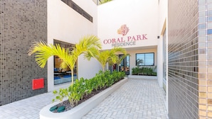 A building with a sign reading 'CORAL PARK RESIDENCE,' surrounded by a paved walkway and greenery. - Beachfront Building With Pool - CPK (Ilhéus)