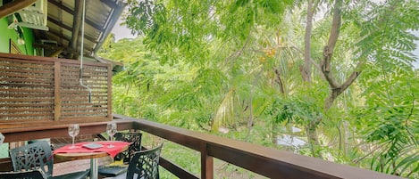 A wooden deck with a table and chairs, overlooking a lush garden with various trees and plants.
