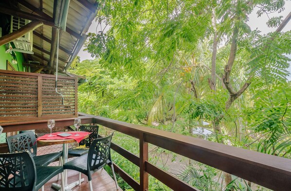Una terraza de madera con una mesa y sillas, con vistas a un jardín exuberante y diverso, lleno de árboles y plantas.