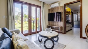 A living room with a sofa, a coffee table, a TV, and a sliding glass door leading to a garden. - House With a Pool 5 Minutes From the Beach Cmv004 (Maraú)