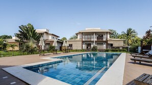 A swimming pool with a wooden deck, surrounded by lush greenery and two-story buildings. - House With a Pool 5 Minutes From the Beach Cmv004 (Maraú)
