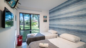 A hotel room with two beds, a large window with a view of a garden, and a wall with a textured mural.